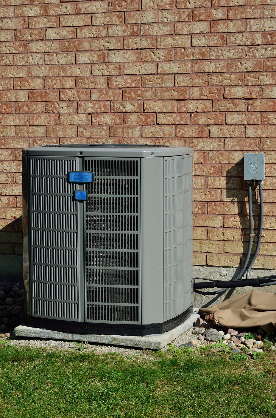 Residential outdoor AC condenser on a concrete pad beside a brick house