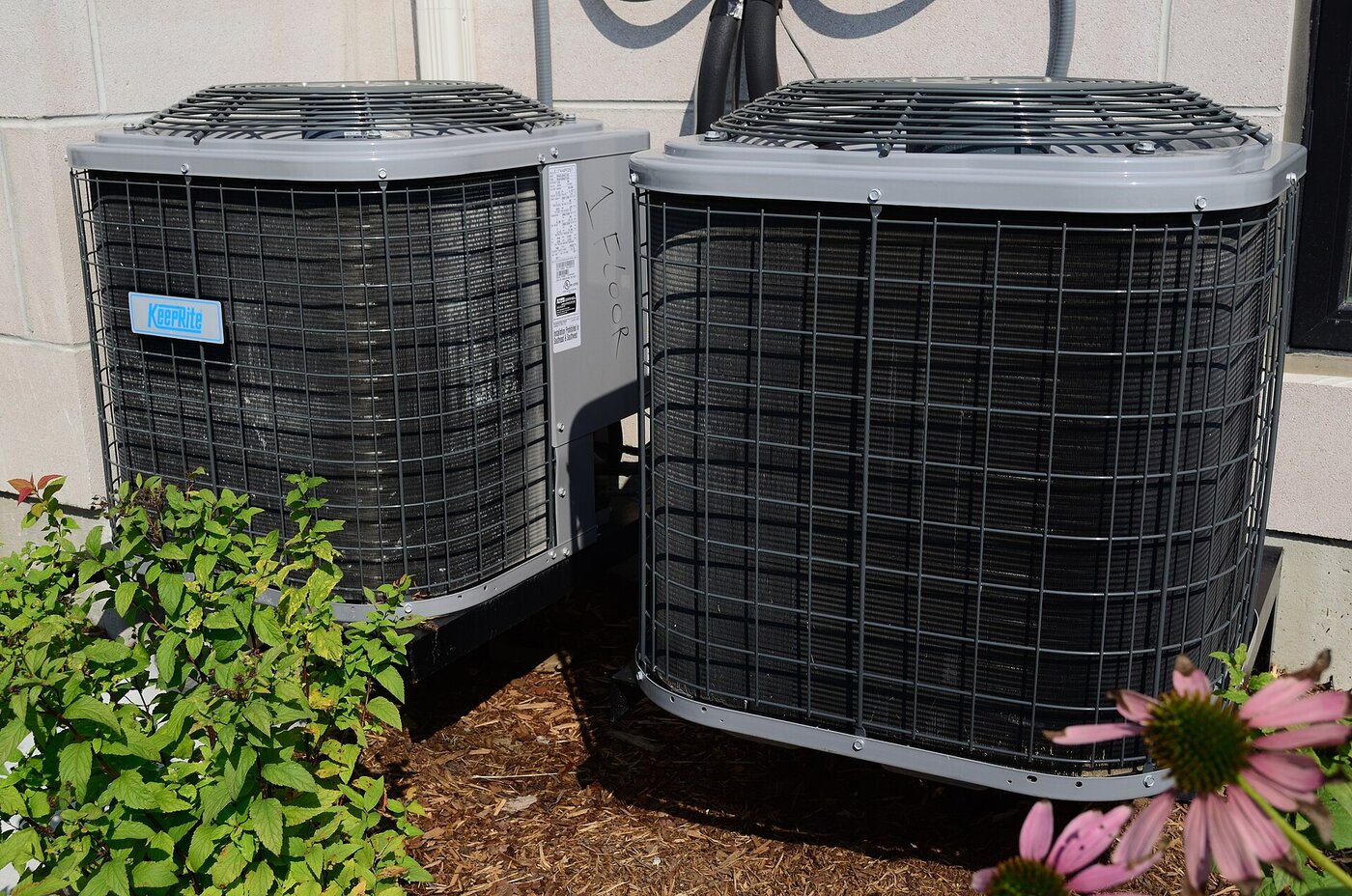 Two residential outdoor AC condensers in a mulched yard bed